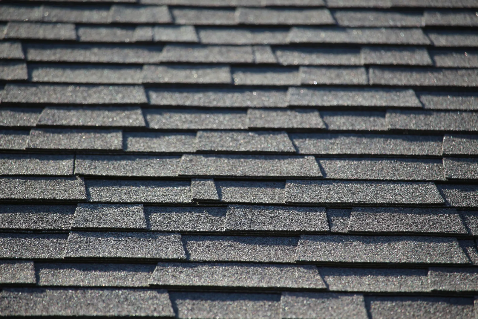 Dark asphalt shingle courses in sunlight casting strong shadows